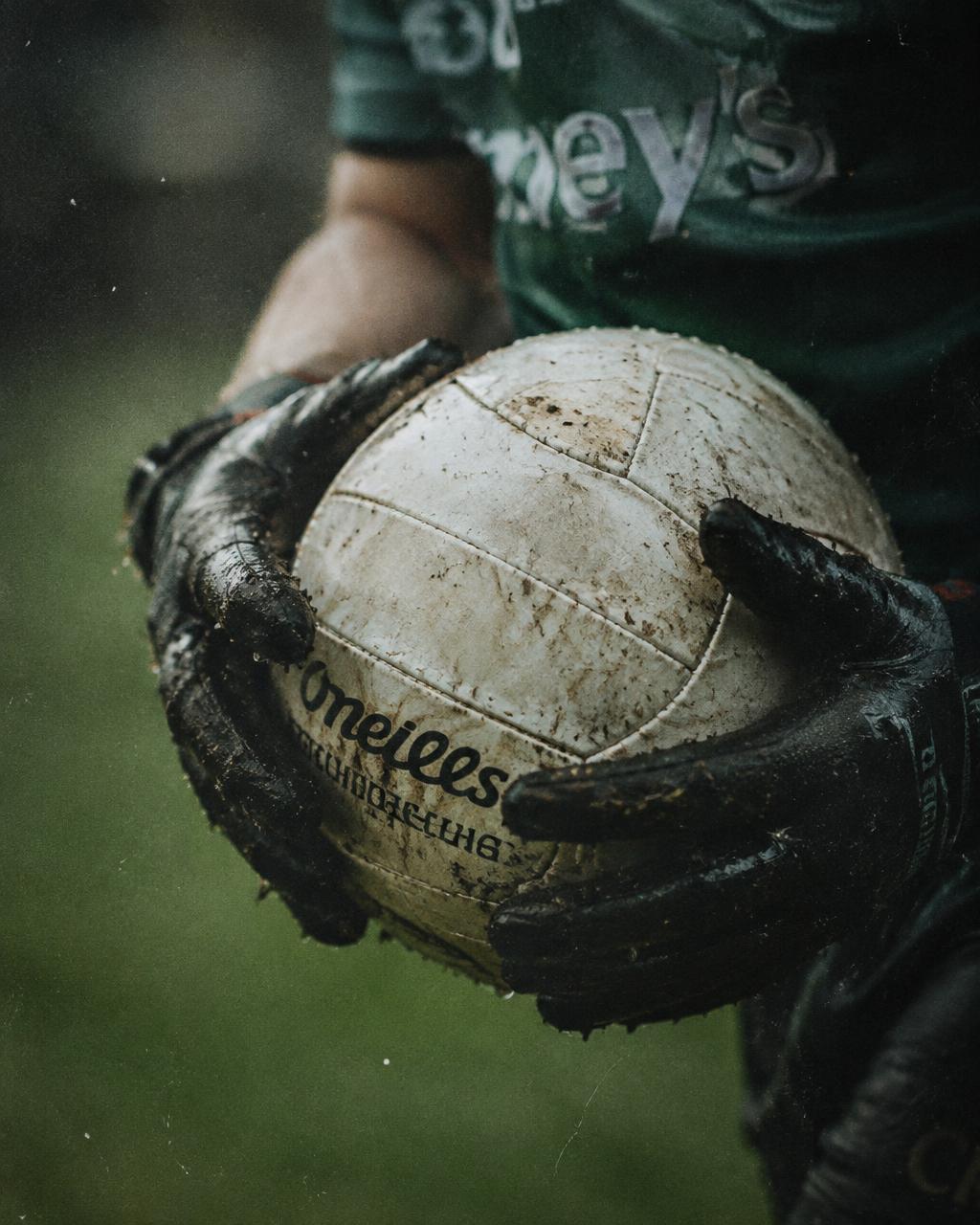 Muddy hands in black grip gloves holding a football